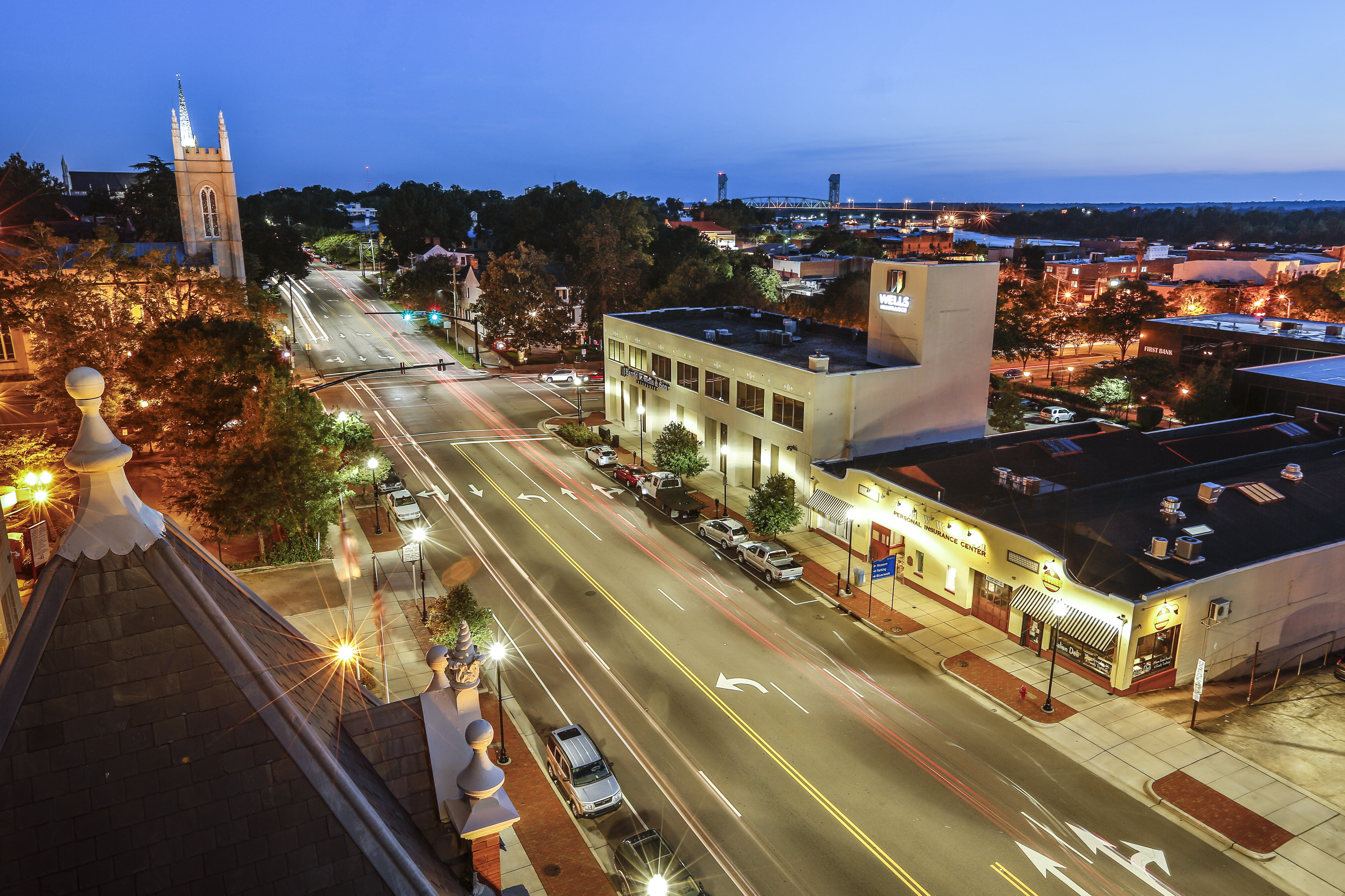 Wells Insurance headquarters in downtown Wilmington, NC, illuminated at dusk with the Cape Fear Memorial Bridge in the background. The image highlights the agency’s presence in the local business community, reinforcing its deep-rooted commitment to serving regional businesses with both local expertise and global capabilities.